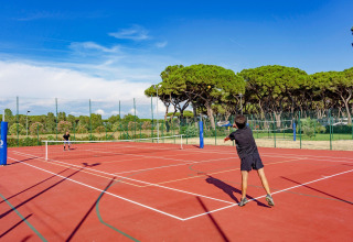 Twee mensen spelen tennis op een buitenbaan omgeven door bomen in Camping Village Roma Capitol, Toscane, Italië.