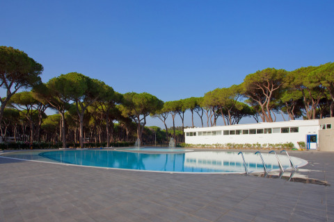 Piscina y edificio moderno rodeados de pinos en Camping Village Roma Capitol, Toscana, Italia.