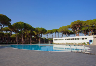 Piscina y edificio moderno rodeados de pinos en Camping Village Roma Capitol, Toscana, Italia.