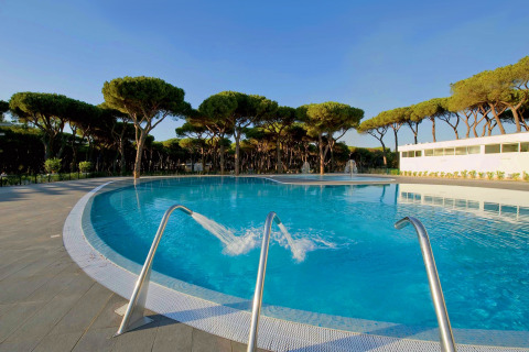 Swimming pool at Camping Village Roma Capitol in Tuscany, Italy, surrounded by pine trees and clear skies.