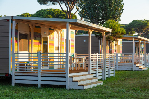 Casas móviles coloridas con terraza en Camping Village Roma Capitol en la Toscana, rodeadas de vegetación.