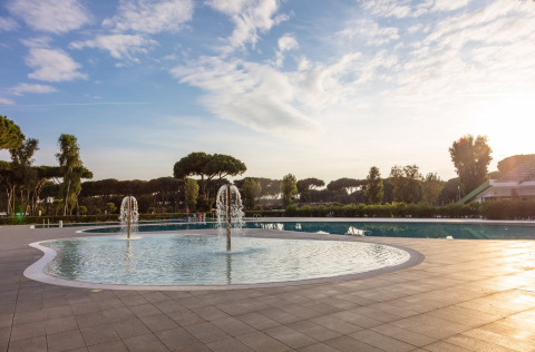 Piscina con fuentes de agua y árboles al fondo en Camping Village Roma Capitol, Toscana, Italia.