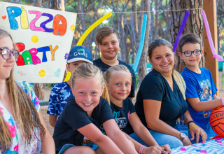 Bambini e un’adulta sorridono a una festa della pizza al Camping Village Roma Capitol in Toscana.