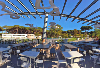 Zona de comedor al aire libre en Camping Village Roma Capitol, con mesas modernas y árboles alrededor.