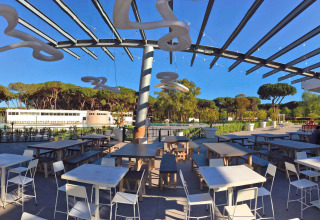 Espace repas extérieur avec tables modernes au Camping Village Roma Capitol, entouré de pins et de verdure.