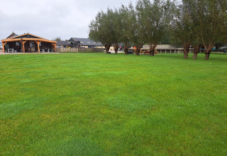 Weite grüne Wiese, Bäume und Holzhütten im Hintergrund bei Camping de Speld in Südholland, Niederlande.