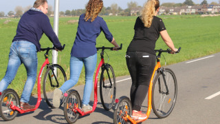 Drei Erwachsene fahren zusammen auf Tretrollern auf einem Weg bei Camping de Speld in Südholland.