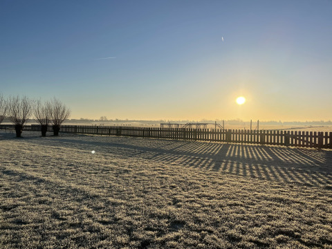 Sonnenaufgang bei Camping de Speld, Raureif auf dem Gras und Schatten vom Zaun, Südholland, Niederlande.