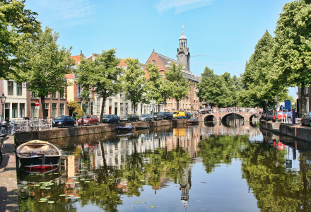 Idyllischer Kanal nahe Nieuwkoop, Südholland, Niederlande, mit Booten, Autos und grünen Bäumen am Ufer.