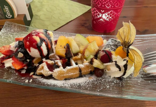 En dessertvaffel med frisk frugt, is, flødeskum og chokoladesauce serveret på en glasfad på et bord.