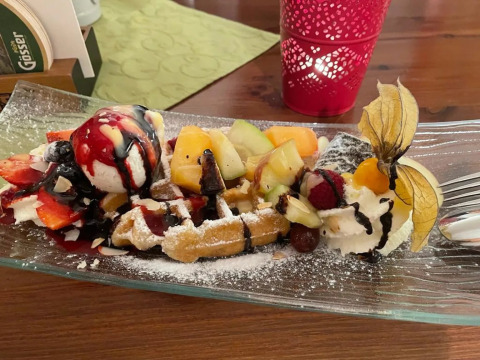 A dessert waffle topped with fresh fruits, ice cream, whipped cream, and chocolate sauce on a glass plate.