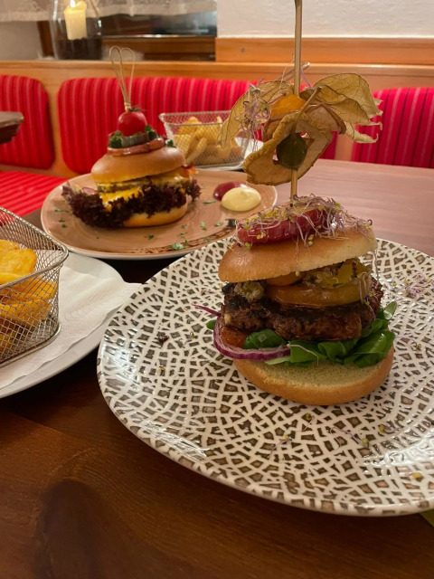 To gourmetburgere med kreative toppings serveret på mønstrede tallerkener på en restaurant med glamping.