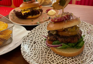 To gourmetburgere med kreative toppings serveret på mønstrede tallerkener på en restaurant med glamping.