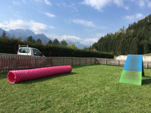Billede af en glamping feriepark med agilitybane for hunde, indhegnet område, bjerge og blå himmel.