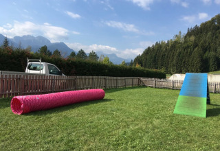 Billede af en glamping feriepark med agilitybane for hunde, indhegnet område, bjerge og blå himmel.