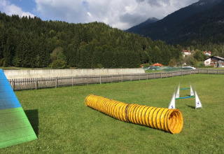 Hundetræningsbane ved en ferielejr med agility-udstyr, grønne bakker og bjerge i baggrunden.