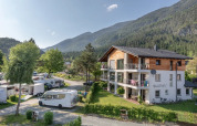 Feriebillede fra en feriepark med campingvogne, bjergudsigt og moderne glampingindkvartering.