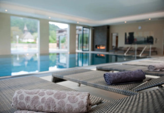 Espace piscine intérieure luxueux avec transats et serviettes roulées dans un parc glamping.