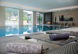Luksuriøs indendørs pool med liggestole og rullede håndklæder på et glamping feriecenter.