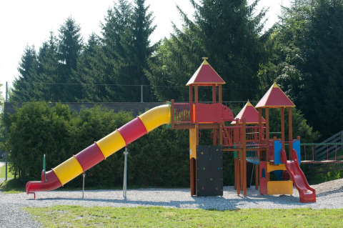 Colorful playground with slides and climbing structures at a holiday park, surrounded by green trees.