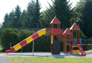 Aire de jeux colorée avec toboggans et tours d’escalade dans un parc de vacances, entourée d’arbres.
