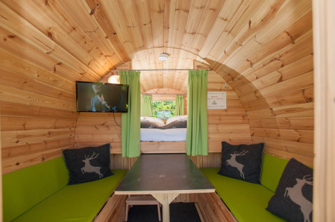 Interno di una confortevole casetta glamping in legno con tende verdi, TV e cuscini cervo in un parco vacanze.