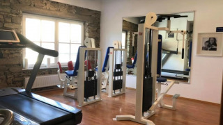 Kleine fitnessruimte in een glampingpark met krachttoestellen, loopband, houten vloer en grote ramen.