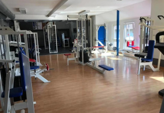 Salle de sport lumineuse avec diverses machines, accessible aux clients d’un parc de vacances glamping.