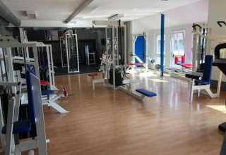Fitnesscenter med forskellige træningsmaskiner og naturligt lys, ideelt til gæster i en glamping feriepark.