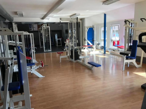 Fitnesscenter med forskellige træningsmaskiner og naturligt lys, ideelt til gæster i en glamping feriepark.