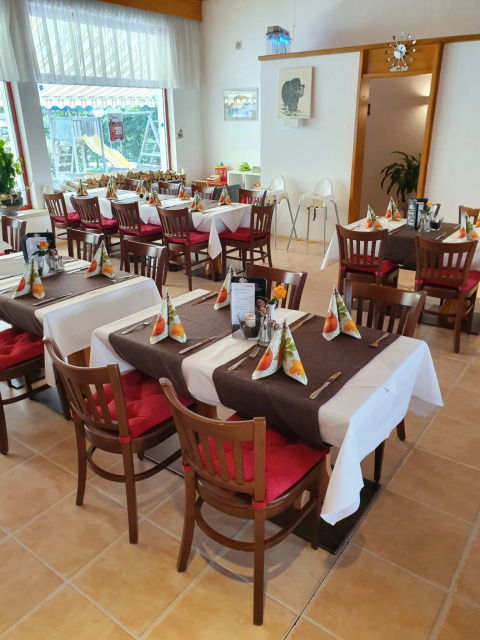 Salle de restaurant chaleureuse avec coussins rouges, serviettes pliées et vue sur une aire de jeux dehors.