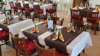 Gezellig restaurant met rode stoelkussens, gedekte tafels en uitzicht op buitenspeeltuin door het raam.