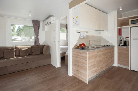 Moderne glamping-indkvartering med stue, køkken og soveområde i feriepark. Lyst og komfortabelt interiør.