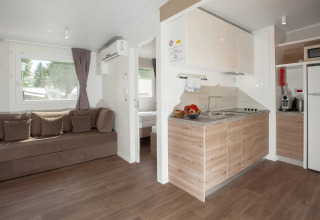 Alojamiento glamping moderno en parque vacacional con sala, cocina y dormitorio. Interior luminoso y acogedor.
