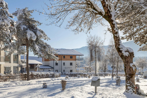 Parque de vacaciones cubierto de nieve con alojamientos glamping, árboles y montañas en un día soleado de invierno.