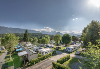 Holiday park with caravans and glamping lodges under sunny skies, surrounded by lush greenery and mountains.