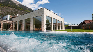 Buitenzwembad bij een modern vakantiepark met glazen gevels en uitzicht op bergen en grasveld.