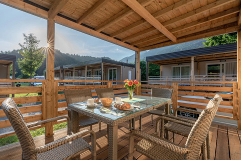 Covered terrace with wicker chairs and breakfast setup, mountain views at a glamping holiday park.