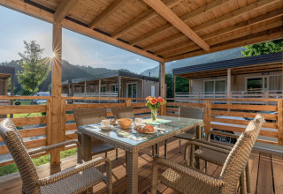 Overdækket terrasse med fletmøbler og morgenmad, udsigt til bjergene ved et glamping-ferieanlæg.