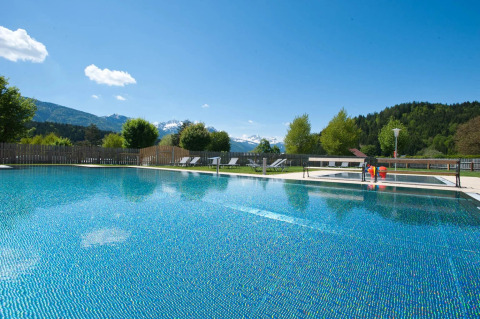Outdoor swimming pool with sun loungers and mountain views at a holiday park offering glamping stays.