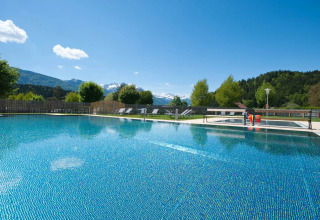 Udendørs swimmingpool med liggestole og bjerge i baggrunden på et feriepark med glampingmuligheder.