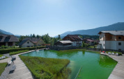 Vue sur une piscine naturelle entourée de terrasses en bois et d’hébergements dans un parc de vacances en montagne.
