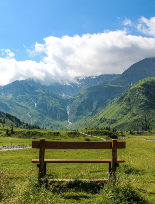 Bankje met uitzicht op groene bergen en dal, onder blauwe lucht, in een vakantiepark met glamping.