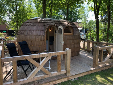Cabaña de madera sobre tarima en Camping Emmen, parque vacacional en Drenthe, Países Bajos, entre árboles.