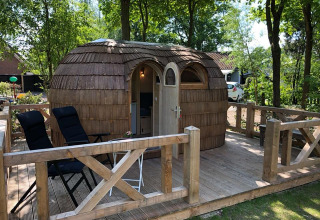 Bijzondere houten hut op terras bij Camping Emmen, vakantiepark in Drenthe, Nederland, te midden van bomen.