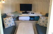 Interieur van IGLO Log Cabin bij Camping Emmen, Nederland, met banken, houten tafel en televisie.