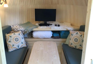 Interiør af IGLO Log Cabin ved Camping Emmen, Nederlandene, med sofaer, bord og tv i træindretning.