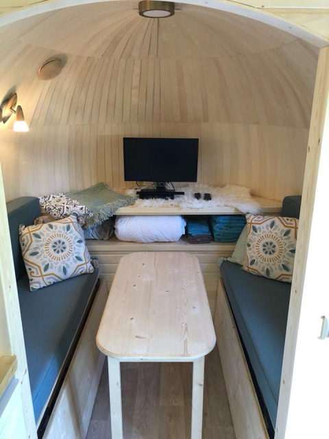 Interior of IGLO Log Cabin at Camping Emmen, Netherlands, showing sofas, wooden table, TV, and decor.