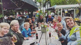 Grupo de personas compartiendo comida al aire libre en Camping Emmen, parque vacacional en Drenthe, Países Bajos.