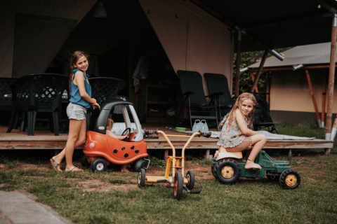 Dos niñas juegan con coches de juguete frente a una tienda en Camping Emmen, parque vacacional en Drenthe, Países Bajos.
